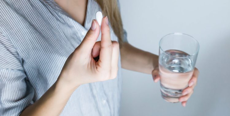 woman holding a pill and glass of water