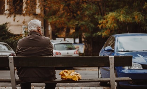 An old man suffering from Parkinson’s sitting on a bench