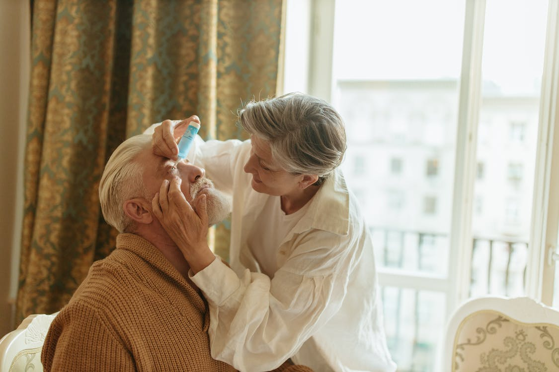 an elderly woman applying eye medicine on a patient