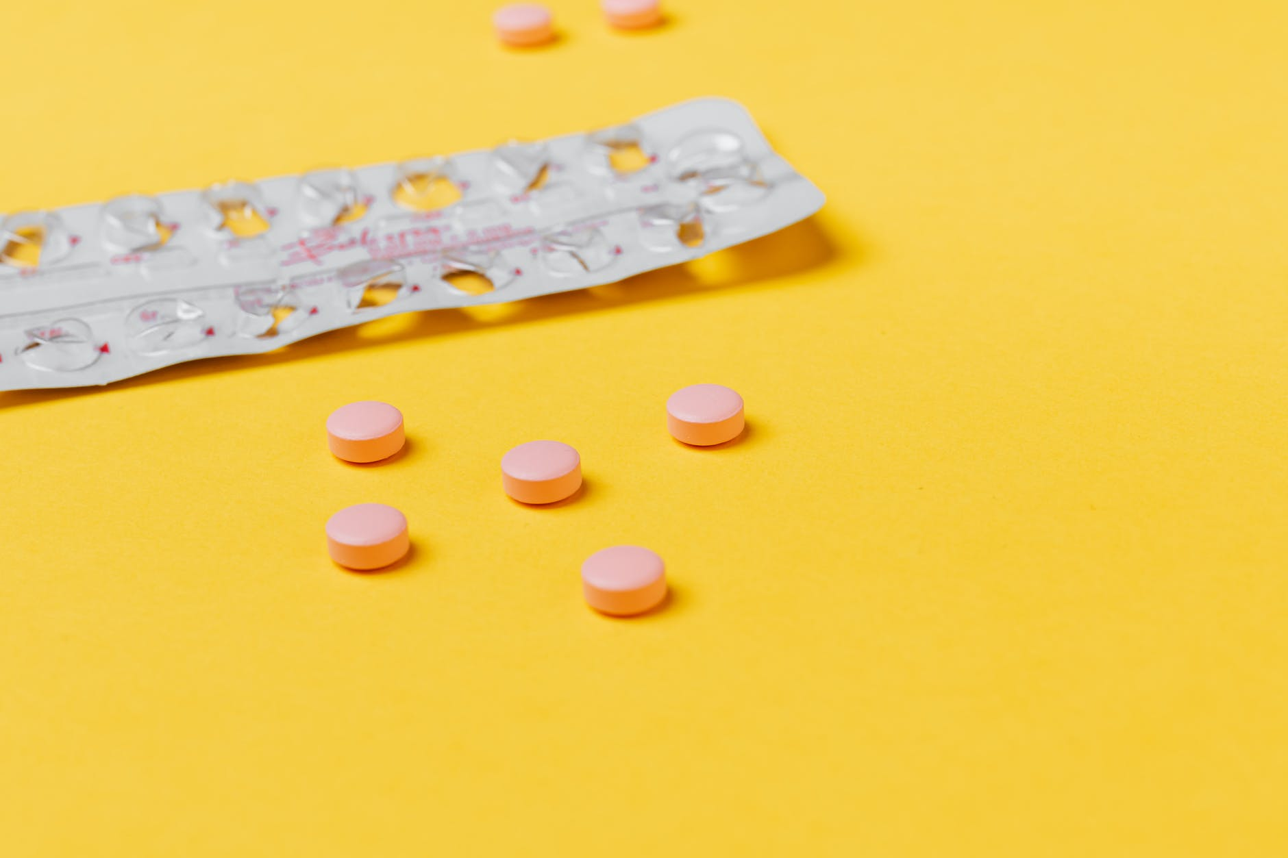 pink pills scattered on a yellow table