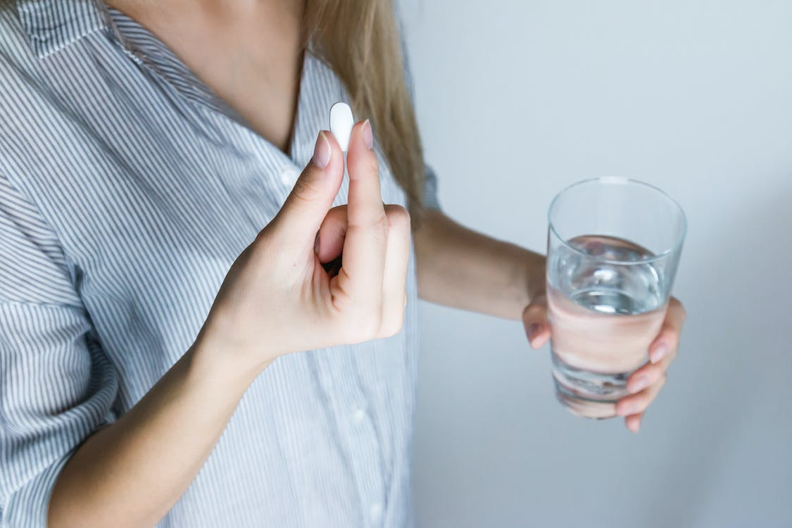 An image of a woman taking a pill with a glass of water in her hand 