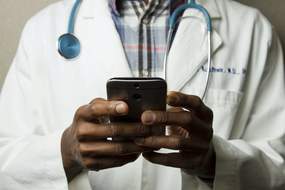 An image of a doctor using his phone with a stethoscope around his neck