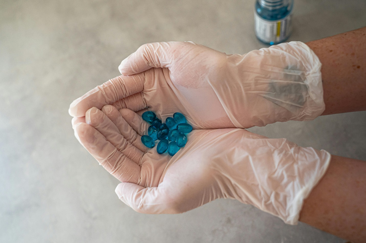 person wearing gloves and holding several blue capsules