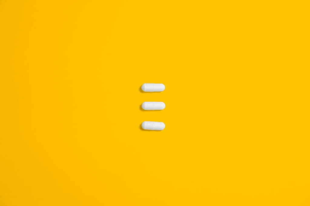 Three white oval capsules on a yellow background.