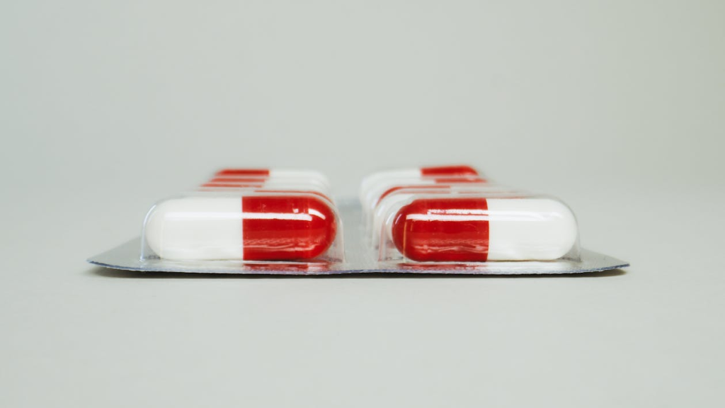 Red and white medicine capsules scattered on a white surface.