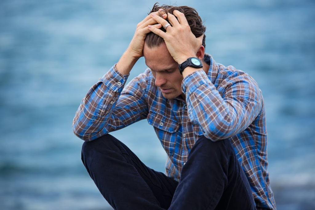 A man in a plaid shirt touching his hair, looking stressed.