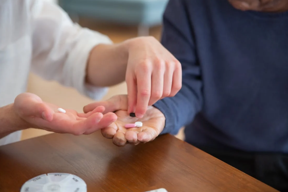 Hands holding and distributing prescription pills on a wooden table