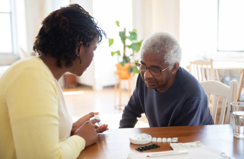 A caregiver assisting an elderly man with his medication at a table