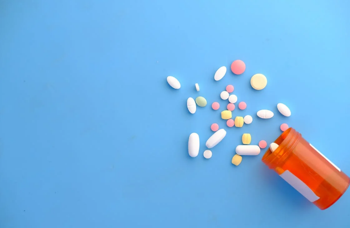 An overturned orange pill bottle spills a variety of colorful pills and capsules