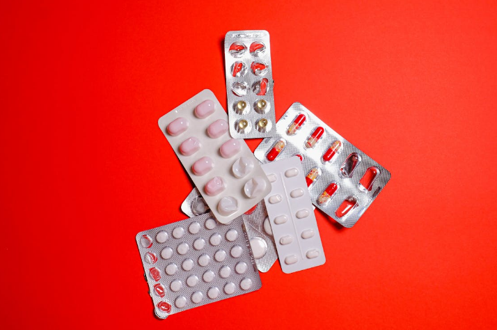 A pile of several different blister packs of pills on a bright red background