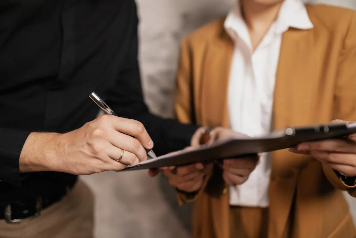 Two people reviewing and signing a document on a clipboard.
