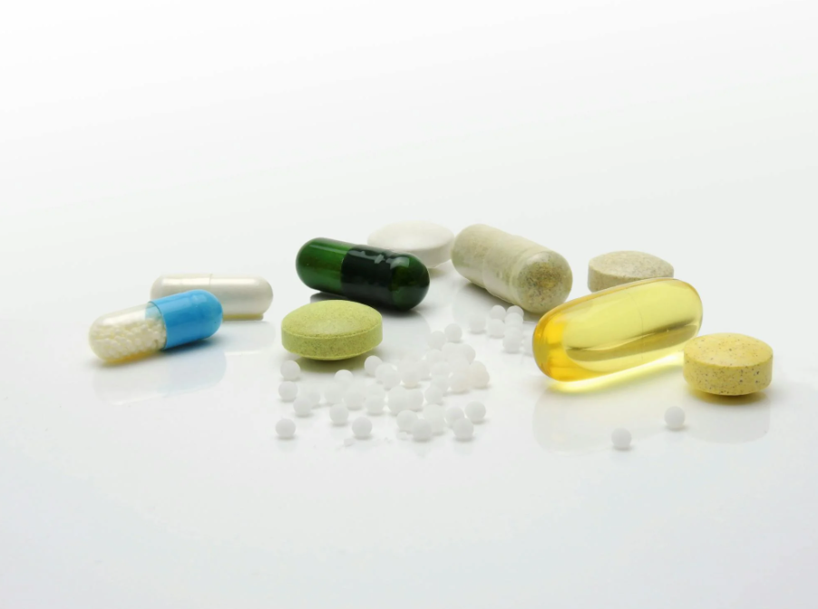 Assorted pills and capsules of various shapes, colors, and sizes on a white surface.