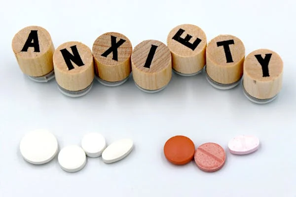Wooden stamps spell "ANXIETY" above two groups of pills.