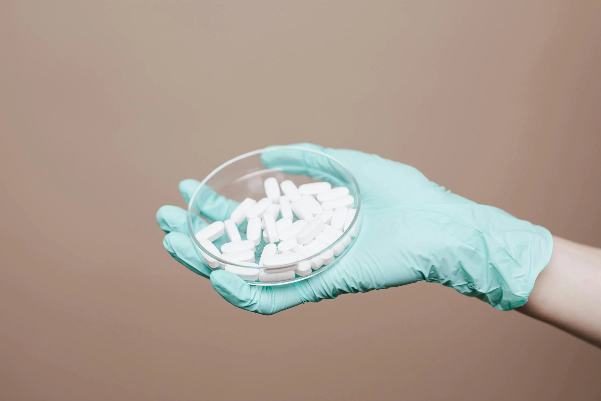 person wearing green latex gloves, holding pills in a round container.