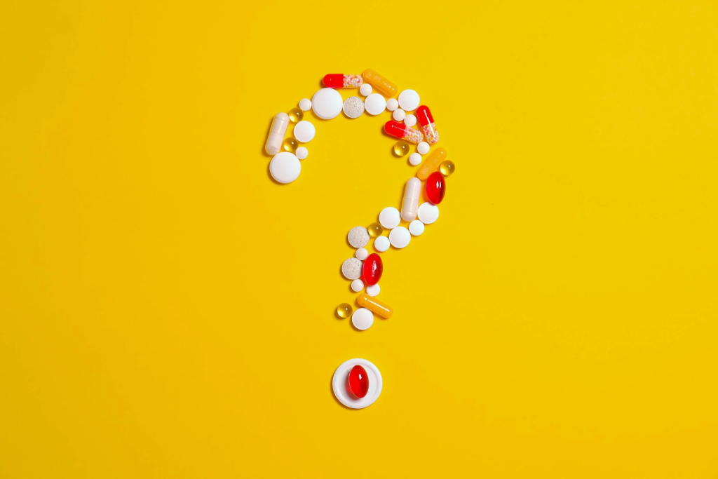 different colored pills and capsules arranged in the form of a question mark on a yellow background.