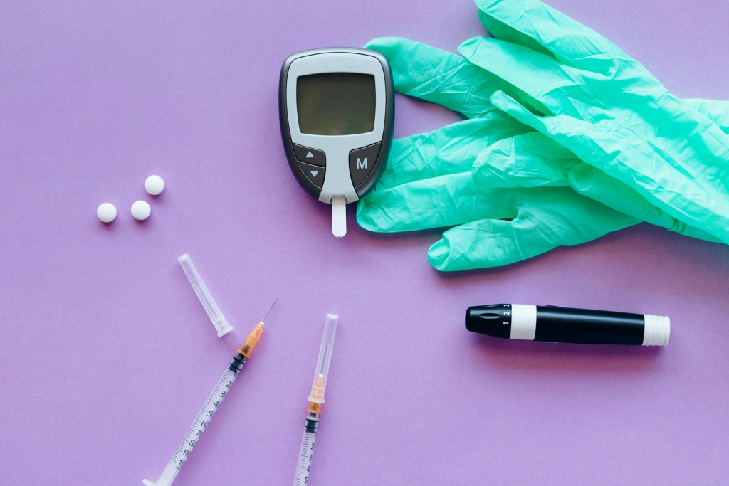 A glucometer, green gloves, white pills, two syringes, and a lancing device.