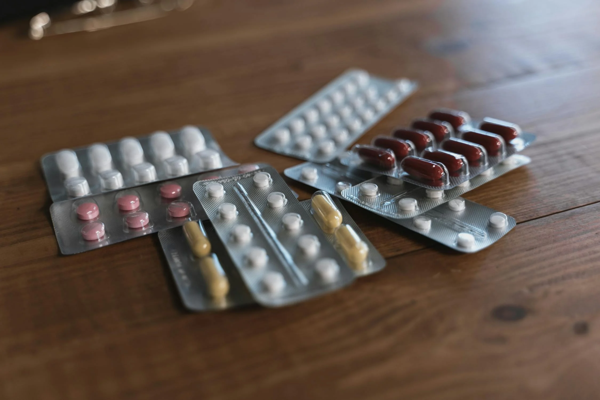Various blister packs with white, pink, yellow, and red pills on a wooden surface.