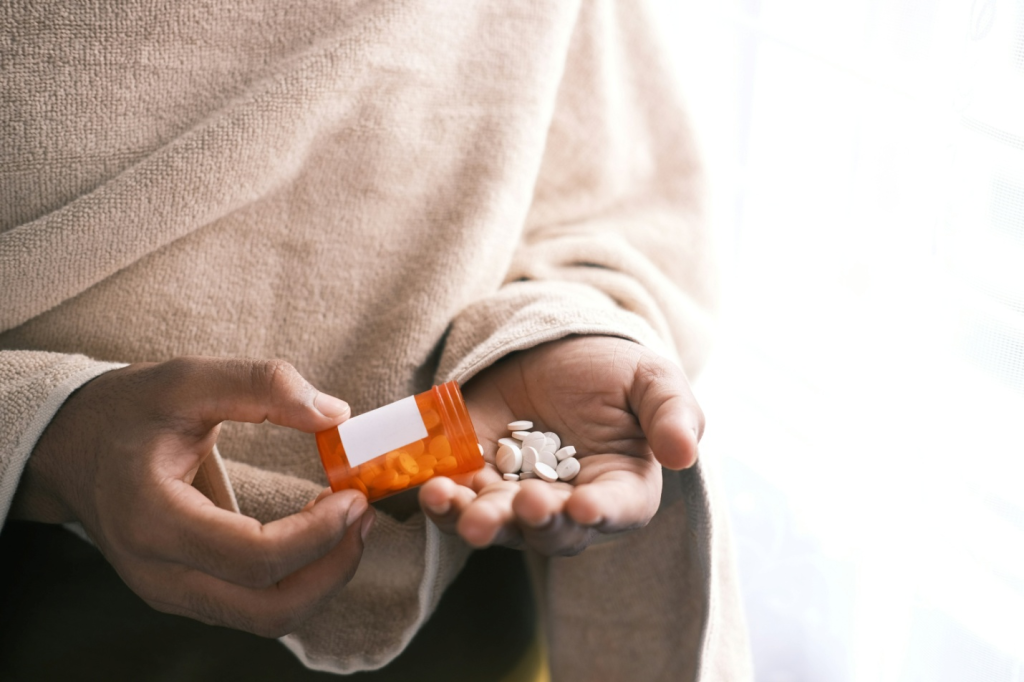 person pouring pills into their hand from an orange bottle