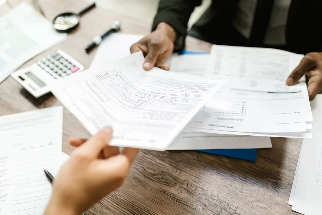 Two people exchanging filled and unfilled forms for approval.
