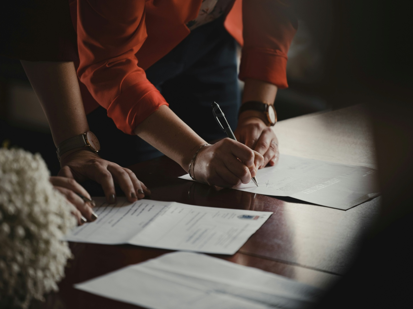 person signing a document placed on a wooden surface