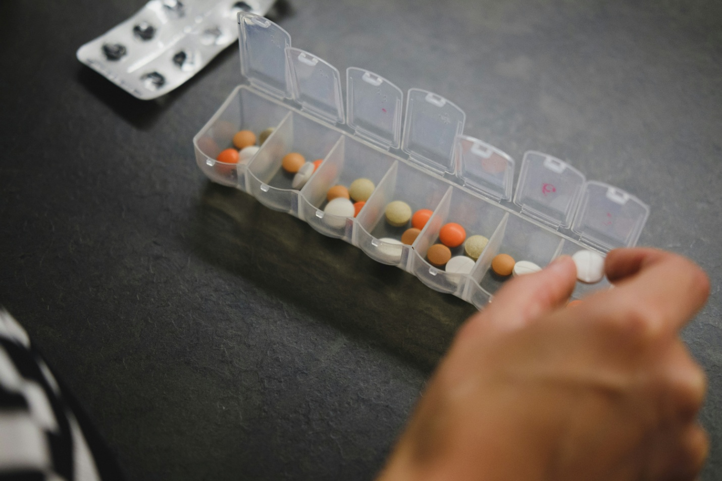 view of a hand sorting pills in a medicine organizer