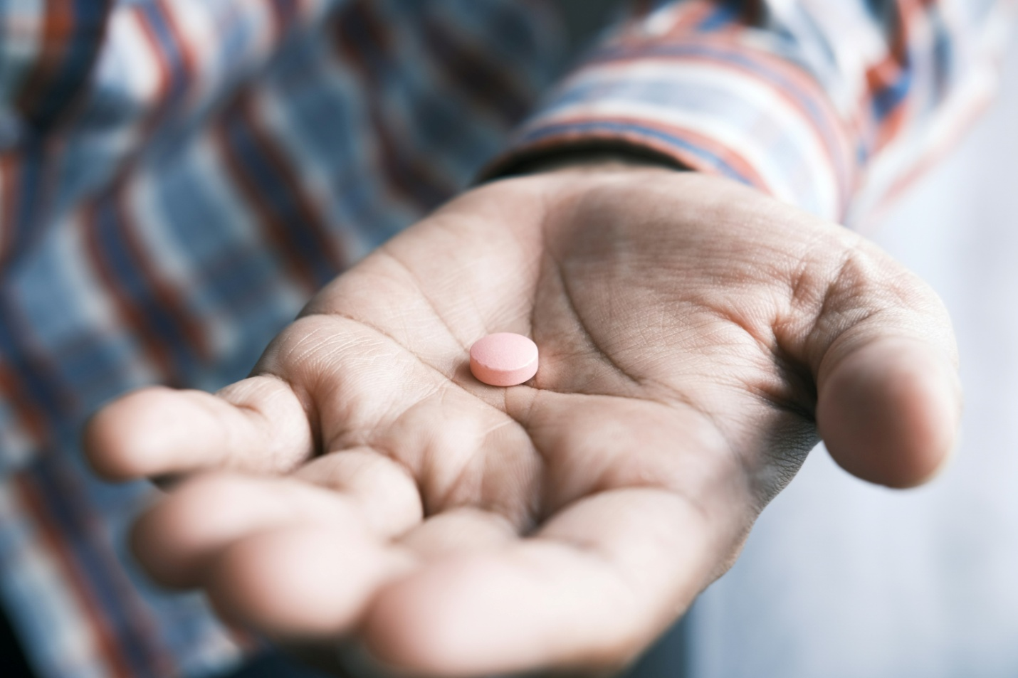 an outstretched hand holding a pink pill