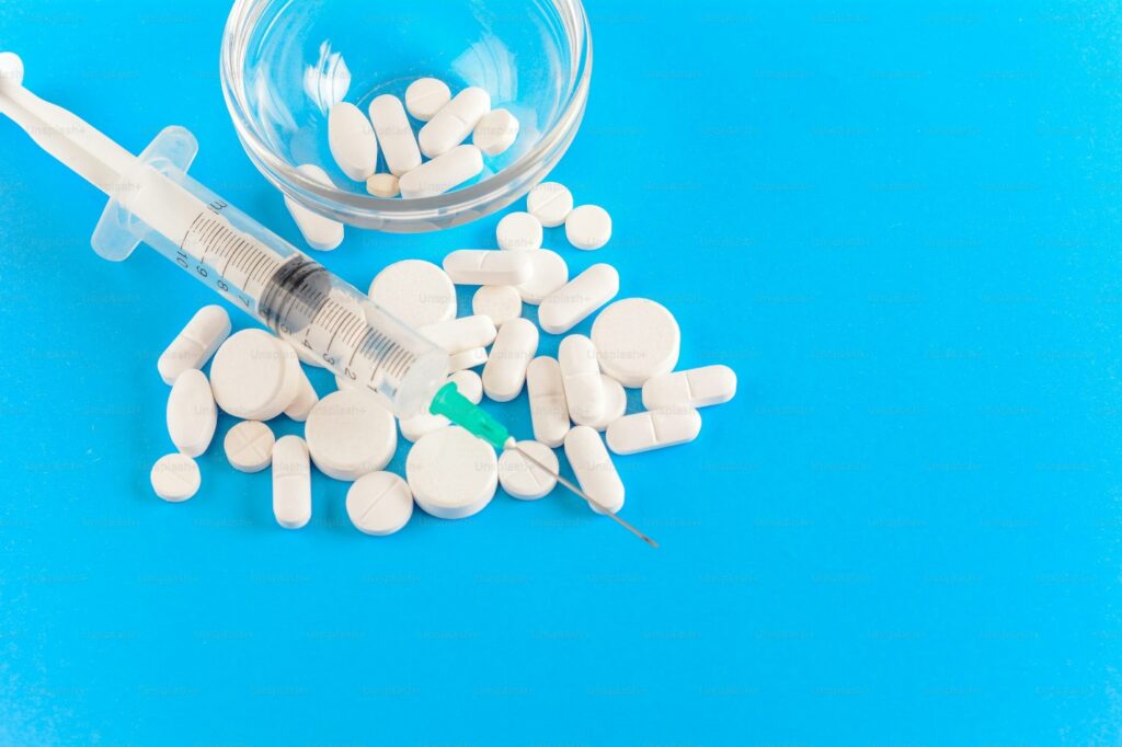 Close up view of needle with drug pills. Light blue background. Drug addiction concept.