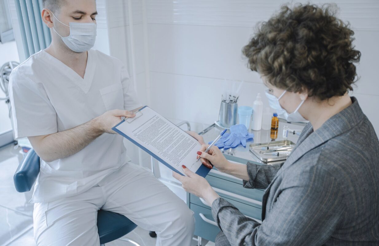 This photo shows a healthcare staff member organizing documents while a patient signs paperwork.
