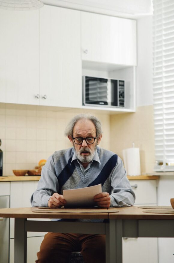 This photo shows a senior reviewing a document at a kitchen table.